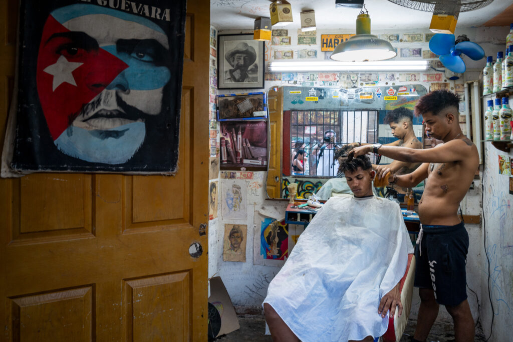Friseursalon in Havanna mit Che-Guevara-Porträt, Friseur und Kunde vor einem Spiegel