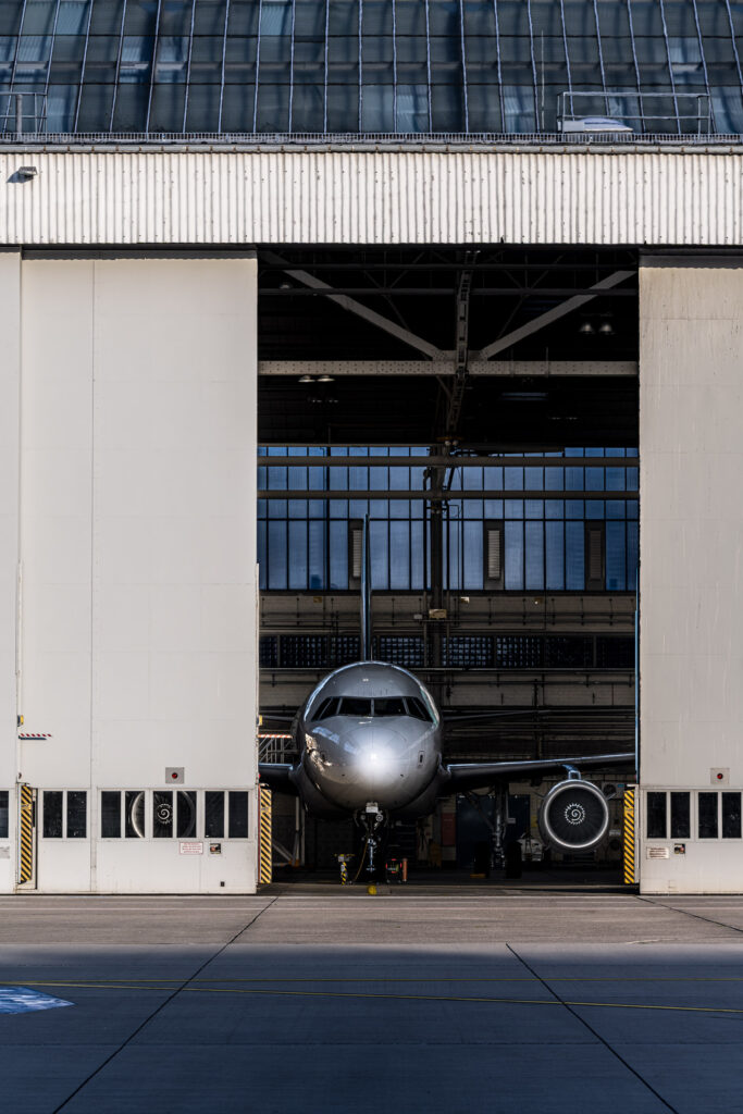 Airbus A320 im Wartungshangar am Flughafen Düsseldorf, symmetrisch zwischen geöffneten Hangartoren fotografiert