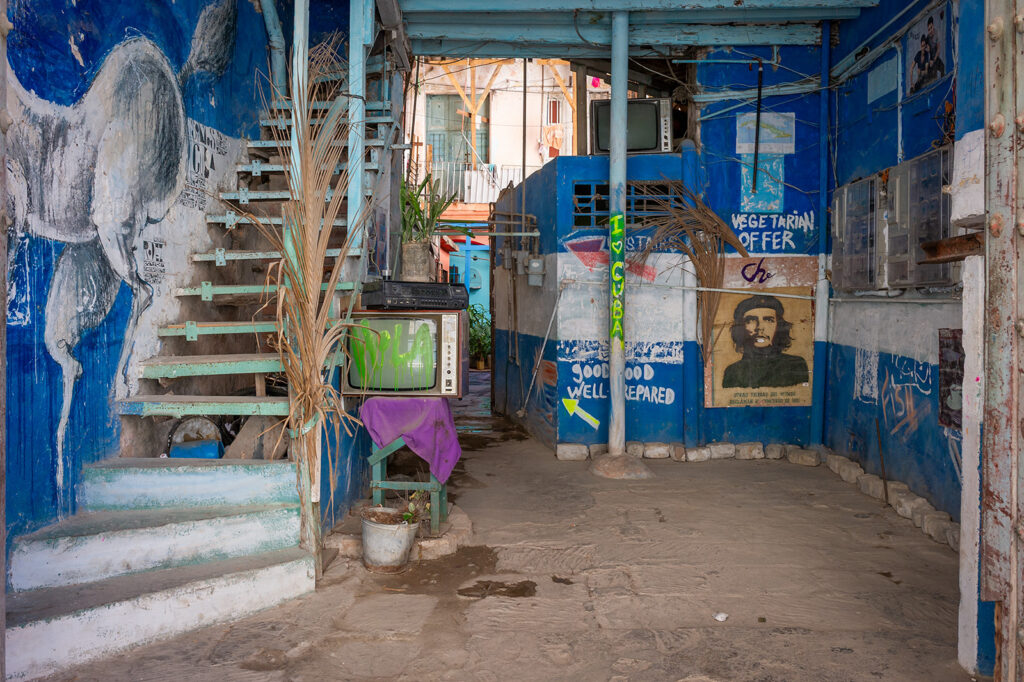 Innenhof in Havanna mit Treppe, altem Fernseher, Che-Guevara-Porträt und blau gestrichenen Wänden
